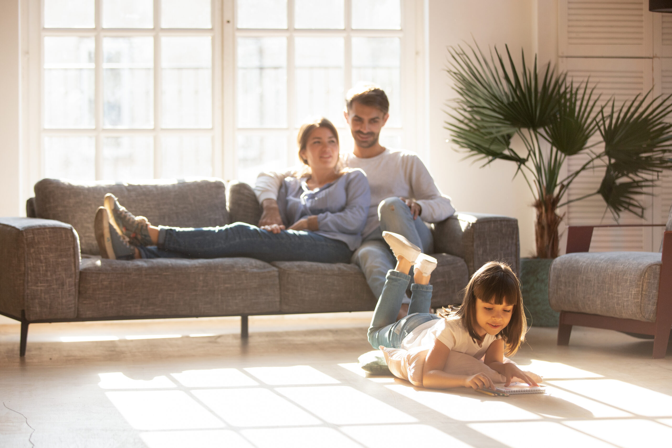 young parents relax on couch watching young child.